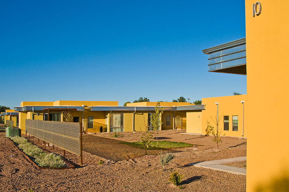 Single-story golden stucco homes and young shade trees around a shared courtyard at Wilshire Gardens, Roswell NM