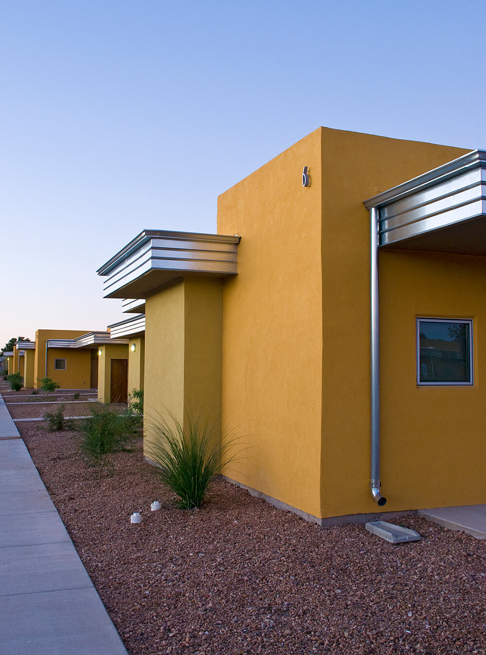 Sidewalk past golden single-story apartment homes with galvanized steel rooflines at Wilshire Gardens, Roswell, New Mexico